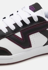 White sneaker with black and purple leather accents, textured patterns, white laces, and purple stitching on the side.