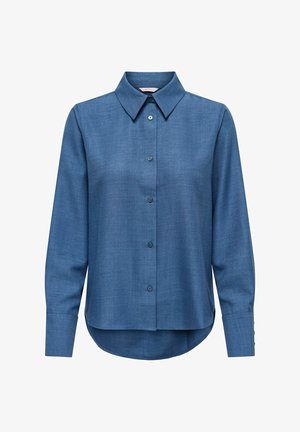 Tumesinist värvi triiksärk tekstuurse kangaga. Omaduseks on pikad varrukad, klassikaline krae ja kõverdatud alumine äär, ees seitse nööpi.