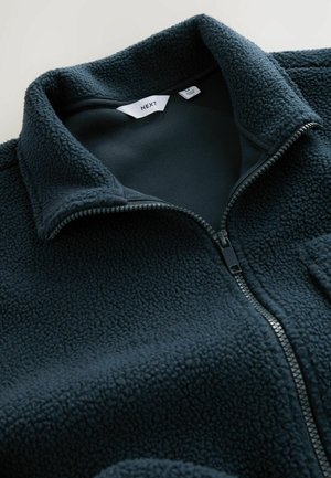 Chaqueta de forro polar con cremallera en azul marino oscuro. Cuenta con un cuello alto, cremallera negra y una tela texturizada con una apariencia suave y cálida.