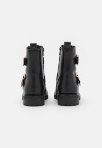 Bottes cheville en cuir noir avec un bout arrondi, une fermeture éclair latérale et deux boucles dorées sur la cheville extérieure. Semelle en caoutchouc épaisse.