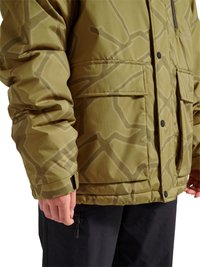 Nahaufnahme einer Person, die eine olivgrün gemusterte Winterjacke mit Klappentaschen und schwarze Hose trägt.
