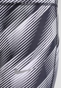Legginsy Nike w czarno-białym wzorze w ukośne paski, wykonane z elastycznego materiału, z przeszywaną talią i małym akcentem logo.
