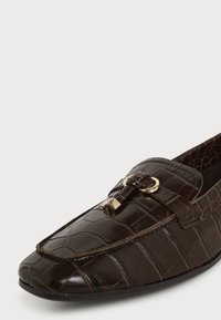 Mocassin en cuir marron foncé à motif crocodile avec une boucle dorée ornant l'avant et un bout rond.