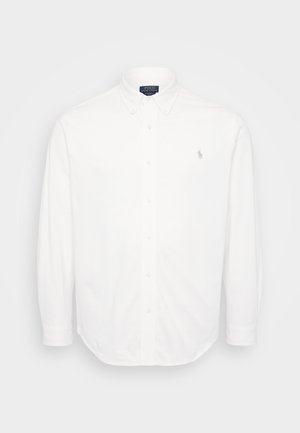 Vit långärmad skjorta med krage med knappar, frontknappar och en liten broderad logotyp på vänster bröst. Tillverkad av bomull.