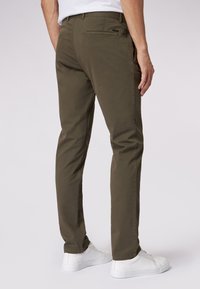 Pantaloni in cotone verde oliva a gamba dritta, con tasche laterali e una tasca posteriore. Abbinati a sneakers bianche.