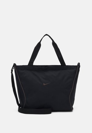 Schwarze Nike Tote-Tasche mit zwei Henkeln, verstellbarem Schulterriemen und kleinem Swoosh-Logo mittig auf der Vorderseite vor einfarbigem Hintergrund.