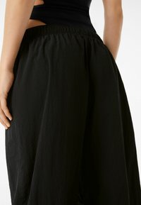 Černé kalhoty vyrobené z lehkého materiálu s texturovaným povrchem, s elastickým pasem a volným, splývavým střihem.