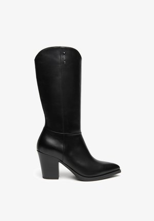 Schwarzer Lederstiefel bis zur Mitte der Wade mit Blockabsatz und spitzer Zehenpartie, mit kleinen Metallnieten nahe dem oberen Rand.