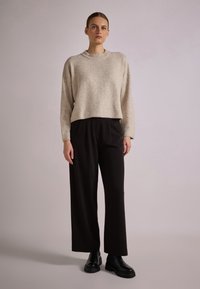 Suéter cropped de color beige claro con escote redondo, combinado con pantalones de pierna ancha negros y botas de tobillo negras. Textura suave, diseño sencillo.