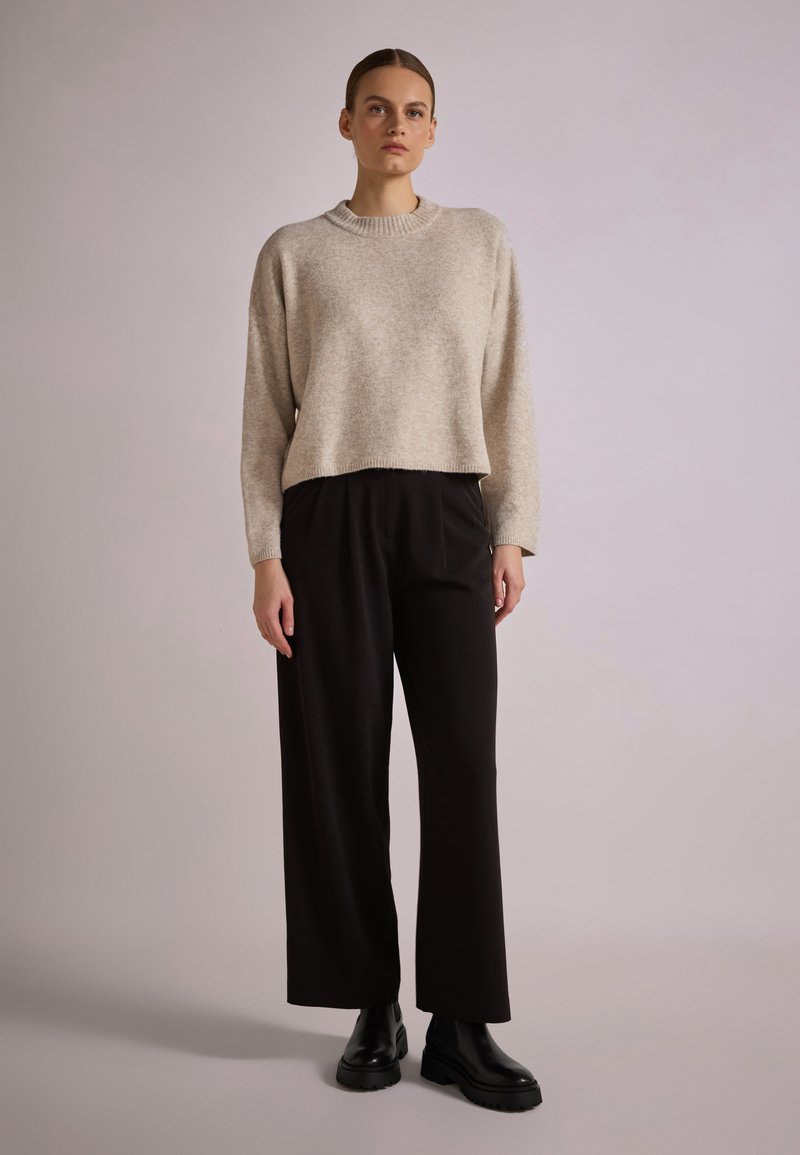 Jasno beżowy sweter typu cropped z okrągłym dekoltem, zestawiony z czarnymi spodniami w szerokim kroju i czarnymi botkami za kostkę. Gładka tekstura, prosty design.