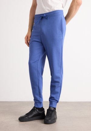 Blue cotton sweatpants with a drawstring waistband, two side pockets, and ribbed cuffs, paired with black sneakers on a neutral background.