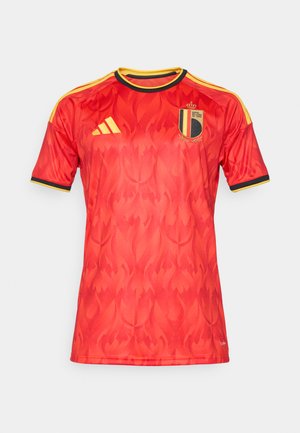 Crvena nogometna majica s diskretnim uzorkom plamena, crnim i žutim obrubom, Adidas logotipom i grbom Kraljevskog belgijskog nogometnog saveza na prsima.