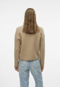 Felpa beige con maniche lunghe e collo rotondo, abbinata a jeans azzurri chiari. Tessuto morbido, vestibilità rilassata e design cropped.