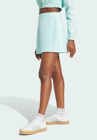 A light mint green athletic skort with white three-stripe designs and logo, paired with white sneakers featuring green accents and gum soles.