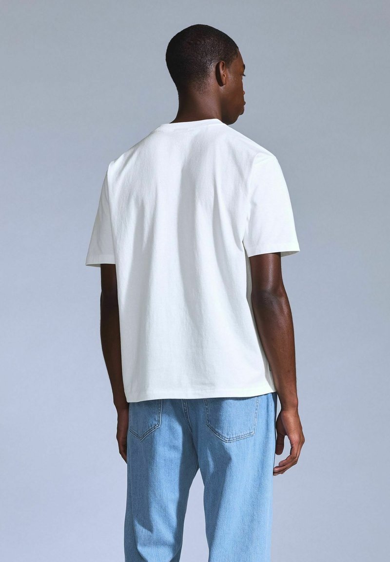 White short-sleeve T-shirt made of cotton, featuring a classic crew neckline and relaxed fit, paired with light blue denim jeans.