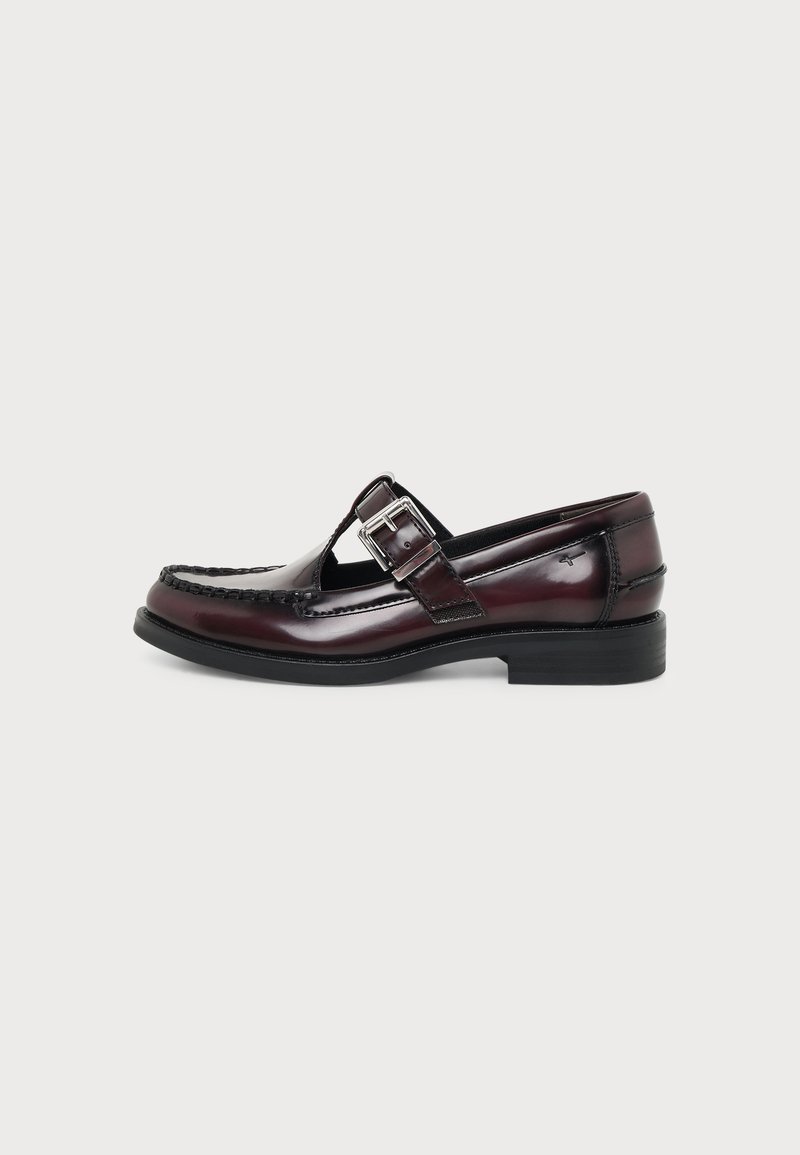Mocassin en cuir marron foncé brillant avec une bride à boucle argentée, une semelle noire et des détails cousus le long des bords.