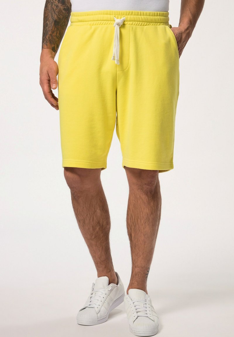 Shorts en coton jaune avec une taille élastique et un cordon de serrage, comportant des poches latérales et une coupe décontractée. Portés avec des baskets blanches.
