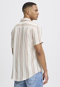 Camisa de botones de manga corta en color crema con rayas verticales marrones, con cuello puntiagudo y dobladillo curvado. Tejido de mezcla de algodón.