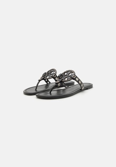 Sandales thong noires avec une semelle plate, présentant un design floral découpé sur la sangle et des accents en métal le long des bords.