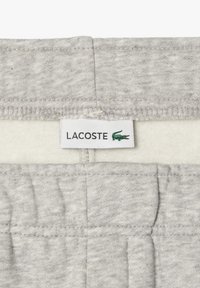 Pantalons de survêtement gris avec une doublure intérieure douce, une taille élastique et une étiquette Lacoste avec un logo de crocodile vert.