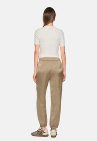 Beige satin joggers with elastic cuffs and two back pockets, paired with a fitted white shirt and animal print sneakers.