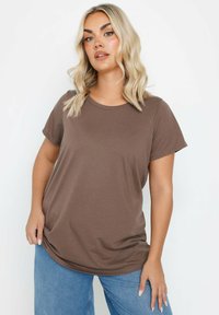 Brun t-shirt lavet af blødt stof, med rund hals og korte ærmer. Pasformen er afslappet, parret med lyseblå denim.