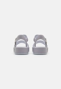 Hallux halli heleksid ja ankle straps'idega hallid platvormsandaalid, vaadatuna tagant valgel taustal.