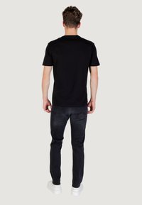 Camiseta de algodón negra de manga corta, con textura suave y un clásico cuello redondo, combinada con jeans oscuros y zapatillas blancas.