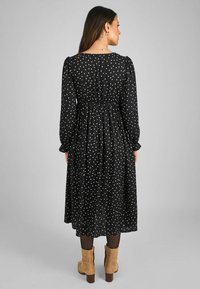 Musta midi-mekko valkoisilla pilkuilla, pitkät hihat, kerrottu vyötärö ja virtaava hame. Yhdistetty vaaleanruskeisiin nilkkureihin.