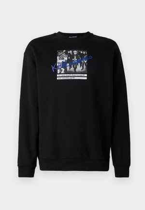 Svart sweatshirt laget av bomull med rund hals. Har et grafisk trykk av en mengde mennesker med blå tekst, "KARL LAGERFELD" som overlapper bildet.