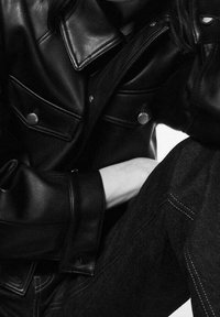 Czarna skórzana kurtka z srebrnymi zatrzaskami, z kołnierzem i przednimi kieszeniami. W zestawie z ciemnymi dżinsami, podkreślająca kontrast tekstur.
