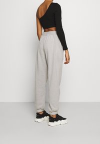 Schwarzes ribbeltes Langarmtop mit asymmetrischem Halsausschnitt, kombiniert mit grauen Sweatpants mit elastischen Bündchen und lockerer Passform, getragen mit schwarzen Sneakers.