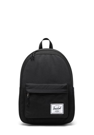 Schwarzer Herschel-Rucksack mit vorderer Reißverschlusstasche und weißem Logo-Patch auf schlichtem weißen Hintergrund.