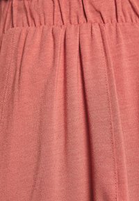 Tessuto morbido di colore corallo con vita arricciata e design a pieghe. Texture liscia con dettagli di cucitura visibili.