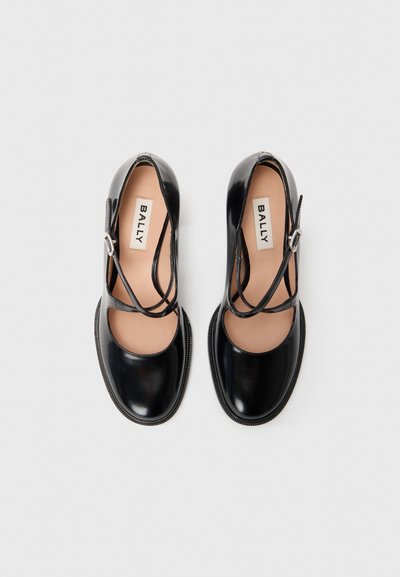 Black patent leather shoes with a rounded toe, cut-out sides, and multiple overlapping straps. Features a textured sole and subtle branding.