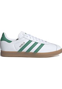 White sneakers with green accents and three striped design. Rubber gum sole, smooth leather upper, and brand name "Gazelle" on the side.