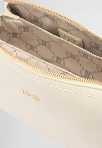 Pochette in pelle color crema con hardware dorato, presenta un interno a due scomparti foderato con un tessuto decorato. Logo impressa sul davanti.