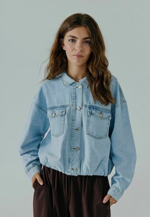 Giacca in denim azzurro chiaro con colletto, chiusura a bottoni e due tasche sul petto. Presenta una vestibilità rilassata e un orlo elasticizzato per un comfort aggiuntivo.