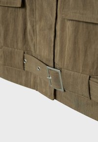 Cintura in tessuto marrone con fibbia rettangolare in metallo, abbinata a un indumento marrone dalla trama simile, mostrata in primo piano.