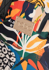 Gevoerde handtas met een mix van levendige kleuren, waaronder oranje, blauw en groen. Bevat een gouden logo plaat en textiel met structuur.