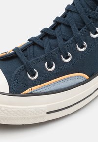 Marine kanvas joggesko med oransje og lys blå detaljer, sølv øyelets, og en hvit gummi tåhette med teksturert såle.