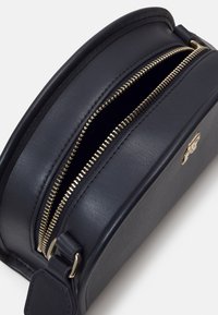 Námořnická kůže kulatá crossbody taška se zlatým zipem a akcentním logem z kovu; hladká textura s plochým profilem.