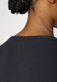 Μαύρο ριμπ ύφασμα τοπ με φαρδύ ντεκολτέ, με ένα μικρό ελάττωμα κοντά στην πίσω περιοχή του λαιμού. Ομαλή υφή και εφαρμοστό σχέδιο.