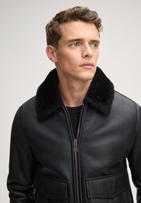 Zwarte leren jack met een faux-fur kraag, rits aan de voorkant, twee opgestikte zakken en een gladde textuur, met een getailleerd ontwerp.