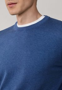 Niebieski sweter z okrągłym dekoltem o gładkiej fakturze, z kontrastującą białą wewnętrzną kołnierzykiem. Dopasowany kroj, miękki materiał.