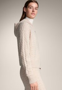 Mikina s kapucí v světle růžové barvě, s kapucí na stažení, žebrovanými manžetami a lemem, volným střihem a texturovanou látkou.