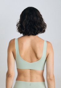 A woman with shoulder-length curly hair is seen from behind, wearing a light green sports bra against a neutral background.