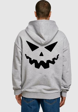 Grauer Hoodie mit einem großen schwarzen Kürbisgesicht-Design auf dem Rücken, das spitze Augen und einen gezackten Mund zeigt. Pullover-Design mit Kapuze.