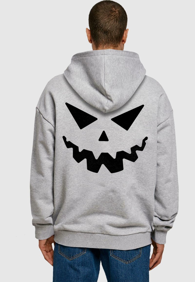 Felpa grigia con un grande motivo a faccia di zucca nera sul retro, caratterizzato da occhi appuntiti e una bocca frastagliata. Design a pullover con cappuccio.
