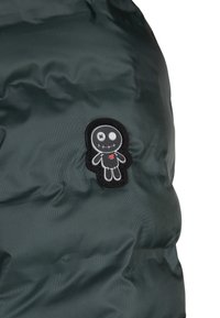 Giubbotto imbottito verde scuro con un tessuto texturizzato, caratterizzato da una toppa in bianco e nero con un personaggio stilizzato e un cuore rosso.